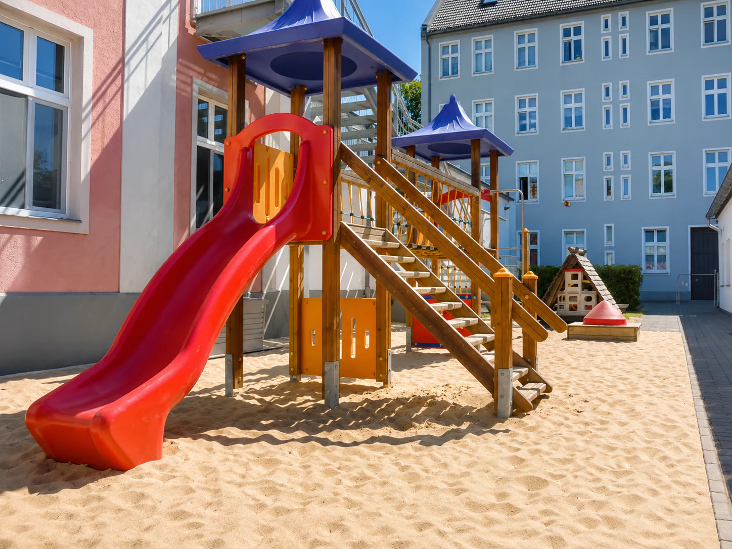 Große rote Rutsche im sandigen Außengelände einer CityKids-Kita